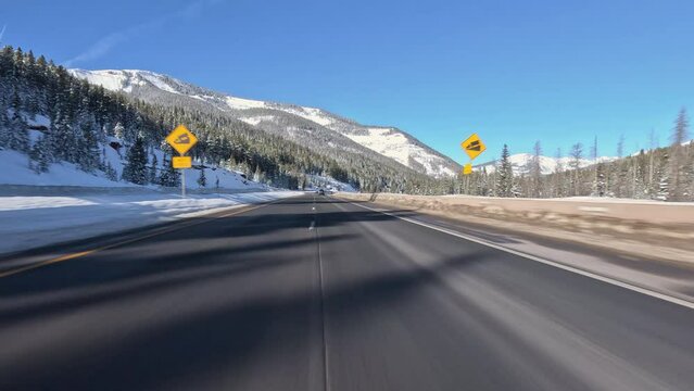 POV driving a car on a highway in high mountains, winter in Colorado, blue clear sky