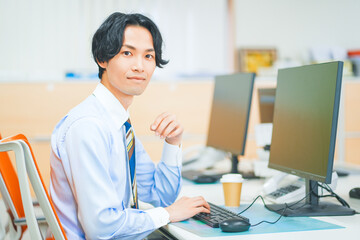 会社でパソコンに向かって仕事をする若いビジネスマン