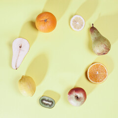 Fruit circle. Row of different fruit and slices. Square composition with long light shadows on gentle pastel yellow bacground.