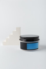 Cream container with empty blue label, mock up template on white background. Face and body skin care cosmetics with concrete decor, copy space