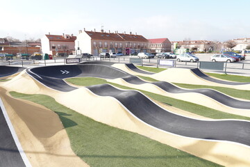 Pump track in black, yellow and with artificial grass; for wheeled vehicles such as bicycles, skates and scooters.