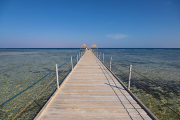 Obraz premium Beautiful beach with a long pier. Yellow sand. Sunny summer day. Blue sky. Transparent beautiful sea.