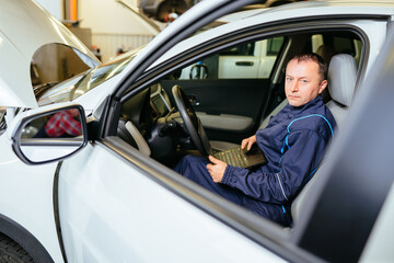 Fototapeta na wymiar Car repair in the workshop. A car electrician is sitting inside the car with open hood.
