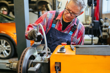 Special equipment automobile brake disk replacement in car repair shop or garage. Mechanic checking car wheel rim.