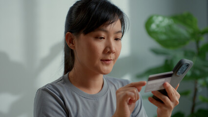Asian woman holding credit card and using smart phone for shopping online at home office.