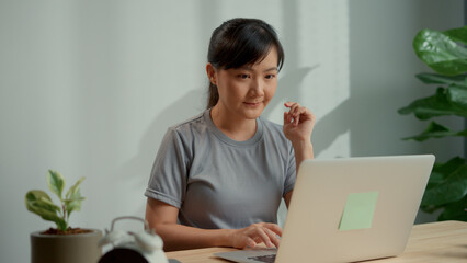 Asian woman happy typing on keyboard using laptop for work at home office.