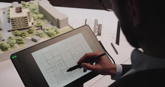 Man architect uses tablet computer and draws project of building