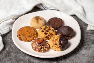 Sweet cookies on a dark background. Varieties of chocolate, hazelnut and pistachio cookies in a plate. close up