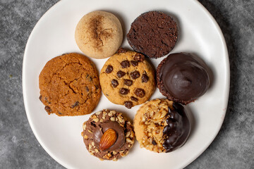 Sweet cookies on a dark background. Varieties of chocolate, hazelnut and pistachio cookies in a plate. Top view