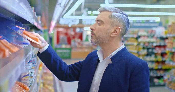 middle-aged man choosing salted salmon in supermarket, shopping in food store, 4K, Prores