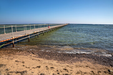Fototapeta na wymiar Beautiful beach with a long pier. Yellow sand. Sunny summer day. Blue sky. Transparent beautiful sea.