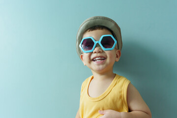 Portrait of Cheerful little Asian boy in yellow sleeveless and blue sunglasses on blue background....