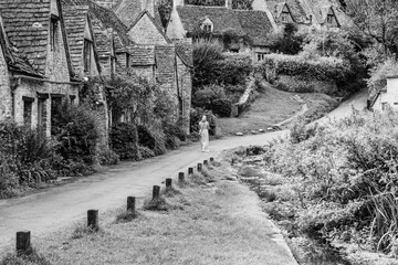 Walking down the path along the traditional row of stone cottage houses on Arlington Row in Bibury village, Gloucestershire, The Cotswolds, England UK