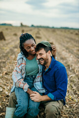 Shot of an affectionate couple sitting together on a farm field. Black woman and a caucasian man sitting in a village field.