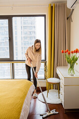 Beautiful young Caucasian blonde housewife cleaning floor in living room. Modern home interior, domestic life