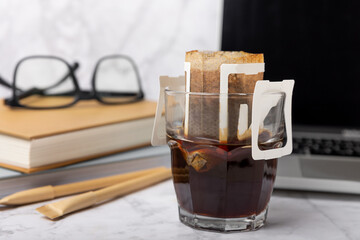 A glass cup of freshly brewed coffee with a handy drip coffee filter on a marble office table. Making freshly brewed coffee at work. Copyspace.Place for text.Coffee making concept.