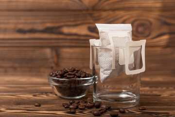 A glass cup of freshly brewed coffee with a handy drip coffee filter on a brown wooden background. Making freshly brewed coffee at home. Copyspace. Place for text.Coffee making concept.
