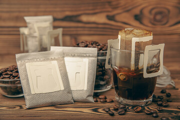 A glass cup of freshly brewed coffee with a handy drip coffee filter on a brown wooden background....
