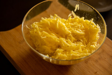 Raw grated potato on wooden cutting board in glass bowl close up. Grate and sliced potatoes pile for swiss potato or pancakes 