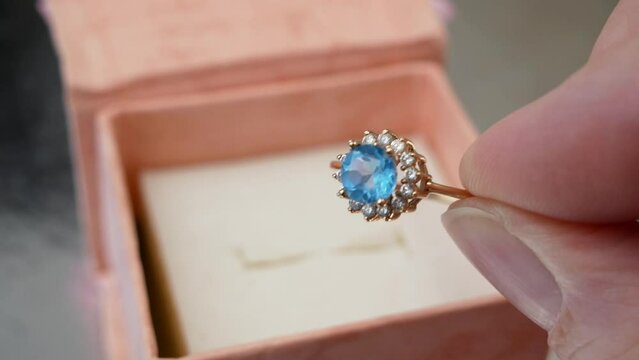 beautiful golden ring with blue big stone and diamonds around in hand near present box