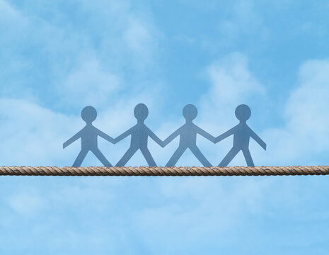 Teamwork mission support. Paper doll walk on the tight rope stretched across the blue sky. Helping friends and working as a team concept. Move forward on the risks carefully. Go ahead together.