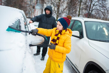 boy helps dad to clear snow from car in winter