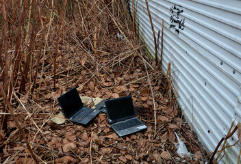 behind a metal fence in the bushes is a secret homeless hacking lair. three laptops are lying on the ground ready to connect. recycling old electrical waste dumped outside the city, personal data