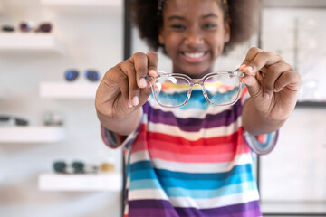Happy American African teen girl with  new eyeglasses frame, showing glasses in the optical store,...