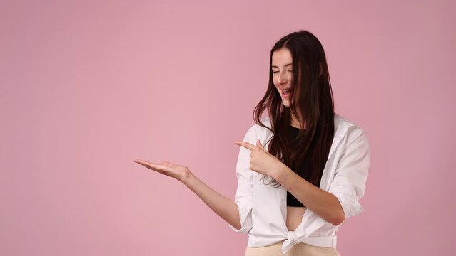 4k slow motion video of one girl pointing at left and showing thumb up over pink background.
