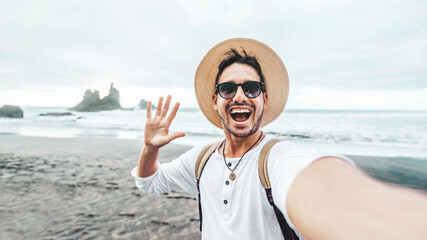 Happy man with backpack taking selfie portrait at the beach - Smiling male tourist travel blogging...