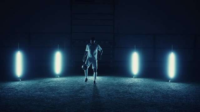 freestyle football player practicing keepie uppie exercise on field in night, silhouette