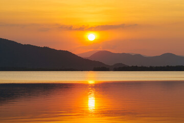 Fototapeta premium Silhouette, beautiful landscape with sunset at coast of the lake in summer. Nature twilight time, reflection, orange sky and yellow sunlight, romantic. Amazing scene at lake in Huai Mai Teng, Thailand