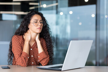 Overtired business woman working inside office with laptop, Hispanic female worker has severe neck...