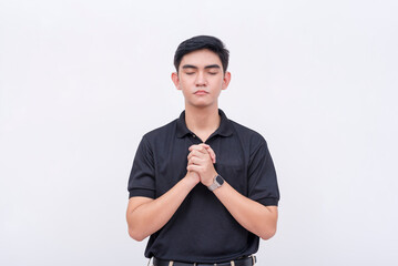A religious young man in a black polo shirt closing his eyes and making a wish or praying. Isolated...