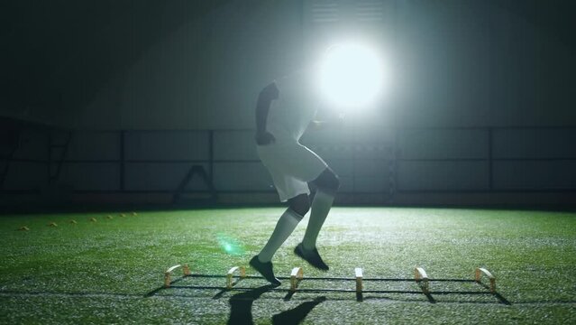 black football player training alone at night, running and jumping in arena with artificial grass