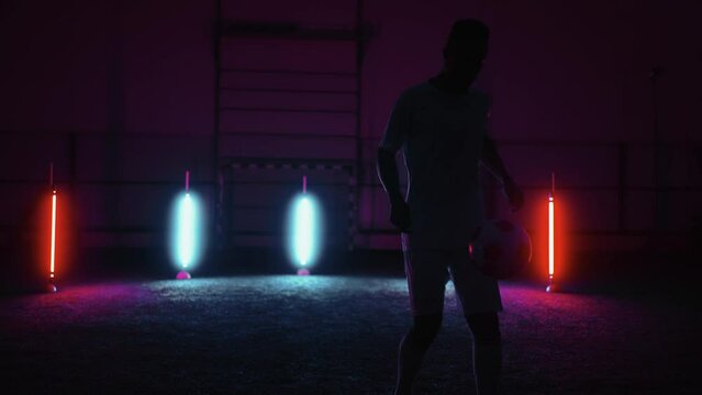 silhouette of african football player in studio, juggling and kicking ball in darkness