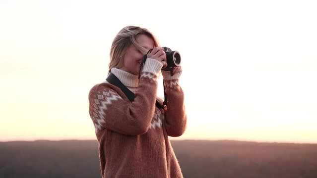 Young photographer stands at the top of a mountain and takes photos of the beautiful pink sunset. Talented content creator looking at the photos of nature.	