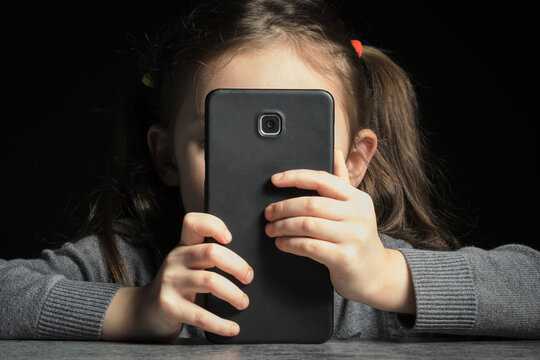 Problem of kids addiction to gadgets, online and screen time. Little girl with big smartphone in her hands.