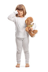 Child in pajamas holding a teddy bear and rubbing eyes