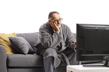 Bored mature man in a bathrobe, sitting on a sofa and watchin tv