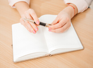 Close up of a woman's hands writing in a notepad placed on a wooden table, home office and work concept, plans and thoughts