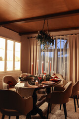Festive table setting for celebration Christmas and New Year holidays in living room. Dining table with traditional dinner meal decorated burning candles, fir branches, xmas baubles, holiday garlands