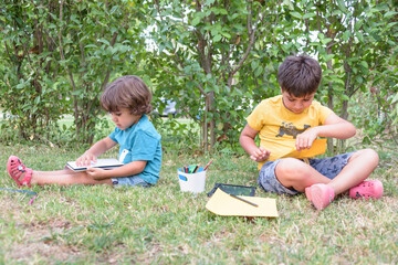 Two student children sitting looking at the notebook in the park. Spring concept and street life.