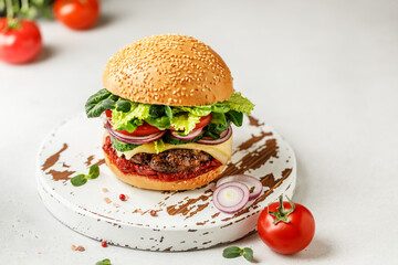 Burger with beef, cheese, green salad, tomato and onion on wooden board. American food concept. Fast food meal.