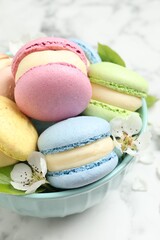 Delicious colorful macarons and flowers in bowl on white table, closeup