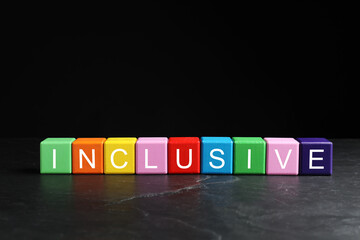 Colorful cubes with word Inclusive on marble table against black background. Space for text