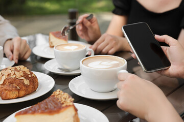 Friends drinking coffee at wooden table in outdoor cafe, closeup