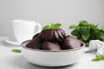 Delicious chocolate covered zephyrs with mint in bowl on white table