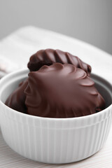 Delicious chocolate covered zephyrs in bowl on white wooden table, closeup