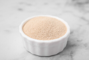 Granulated yeast in bowl on white marble table, closeup